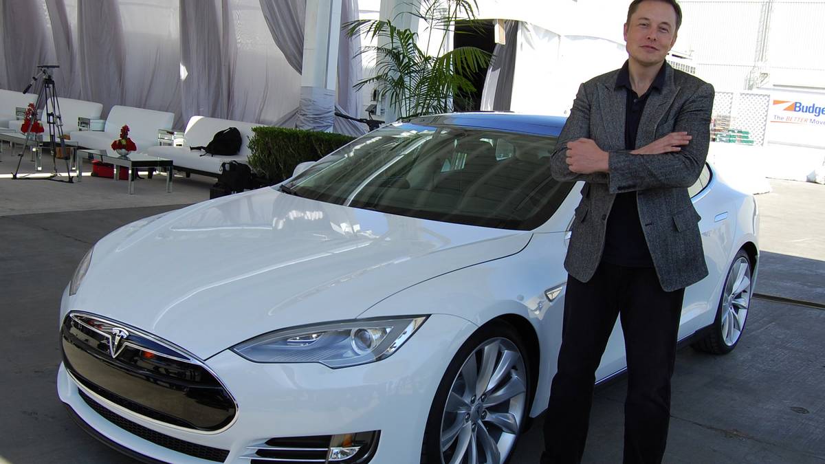 Elon Musk standing next to a white Tesla car